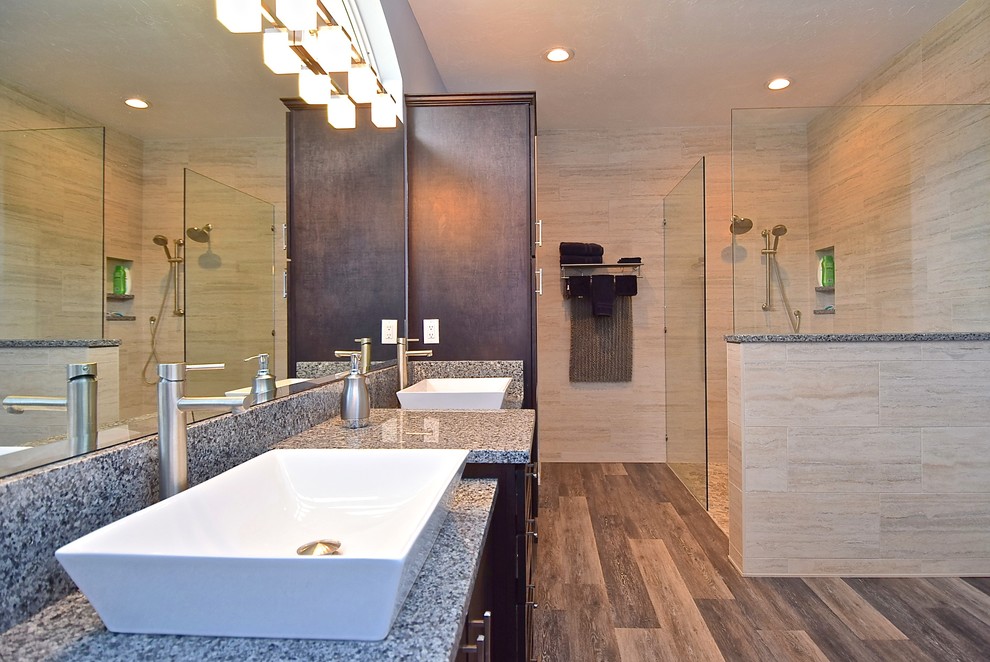 This is an example of an expansive transitional master bathroom in Tampa with vinyl floors, a vessel sink, grey floor, an open shower, recessed-panel cabinets, brown cabinets, a double shower, beige tile, porcelain tile and granite benchtops.