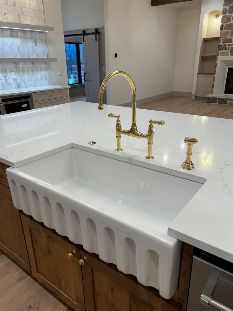 Large transitional l-shaped light wood floor and shiplap ceiling kitchen photo with a farmhouse sink, shaker cabinets, beige cabinets, quartz countertops, gray backsplash, marble backsplash, stainless steel appliances, an island and white countertops