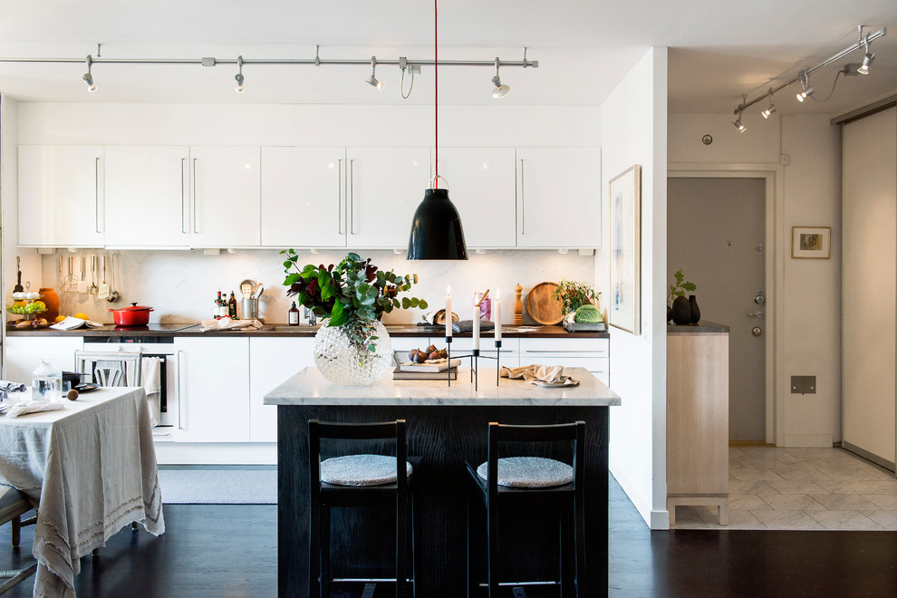 Photo of a mid-sized scandinavian single-wall eat-in kitchen in Stockholm with flat-panel cabinets, white splashback, dark hardwood floors, with island and marble benchtops.