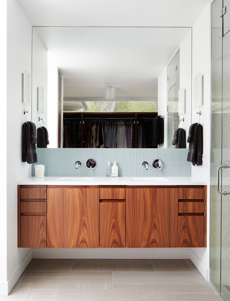 Midcentury bathroom in Chicago with an undermount sink, flat-panel cabinets, dark wood cabinets, blue tile, glass tile and white walls.