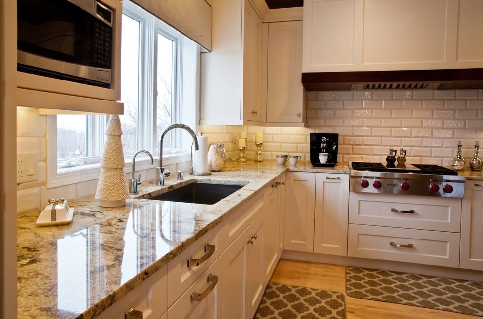 Open concept kitchen - large transitional l-shaped light wood floor and brown floor open concept kitchen idea with an undermount sink, shaker cabinets, white cabinets, granite countertops, white backsplash, subway tile backsplash, paneled appliances and an island