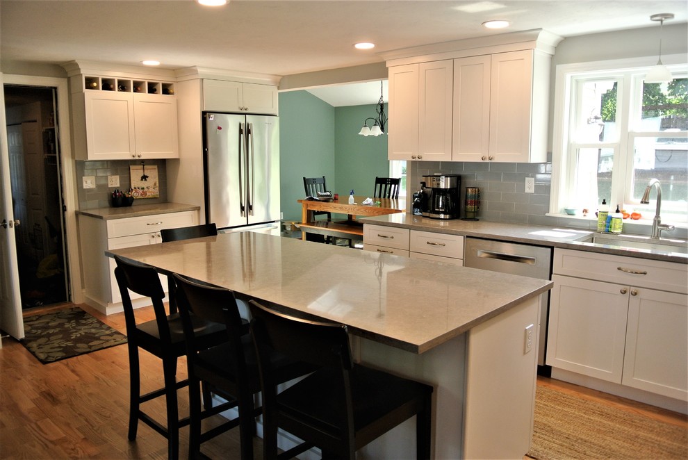 Example of a transitional light wood floor kitchen design in Boston with an undermount sink, shaker cabinets, white cabinets, quartz countertops, gray backsplash, subway tile backsplash, stainless steel appliances, an island and gray countertops