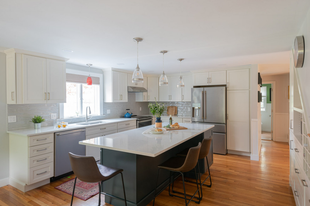 Inspiration for a large transitional l-shaped light wood floor and brown floor eat-in kitchen remodel in Boston with an undermount sink, shaker cabinets, white cabinets, quartz countertops, gray backsplash, ceramic backsplash, stainless steel appliances, an island and white countertops
