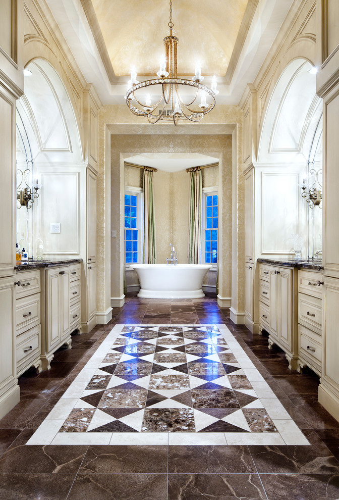 Photo of a traditional bathroom in Houston with raised-panel cabinets, beige cabinets, a freestanding tub, beige walls and brown floor.