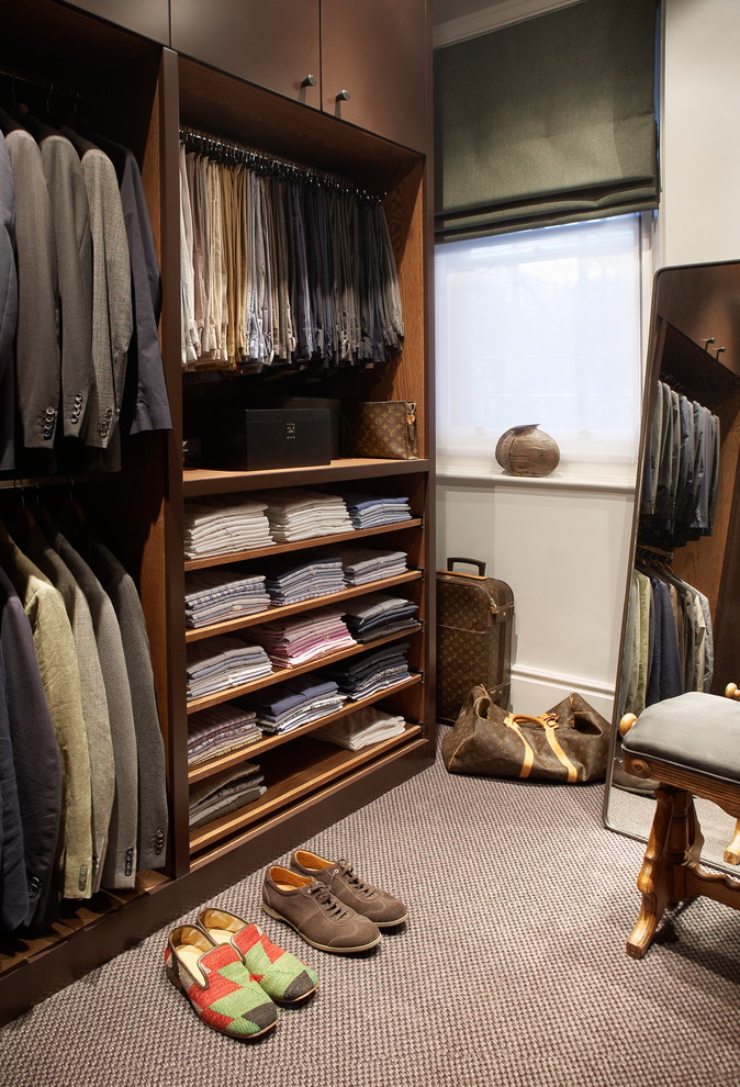 Large traditional men's walk-in wardrobe in London with open cabinets, dark wood cabinets, carpet and brown floor.