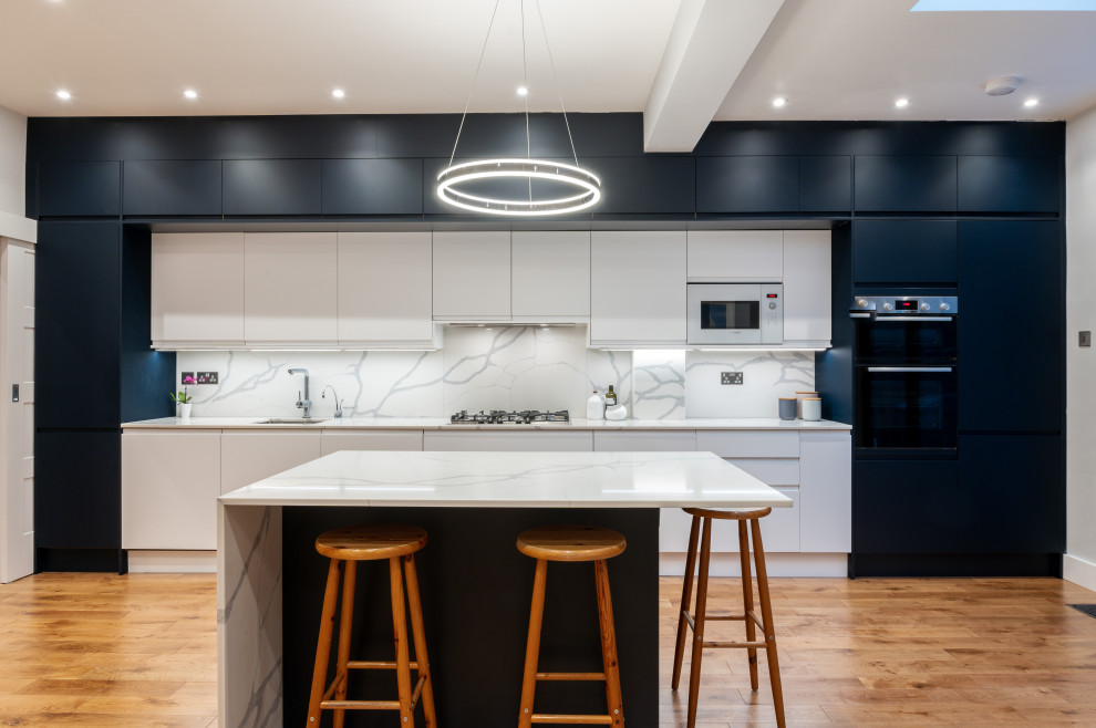 Photo of a contemporary open plan kitchen in London with flat-panel cabinets, blue cabinets, quartzite benchtops, white splashback, panelled appliances, medium hardwood floors, with island and white benchtop.