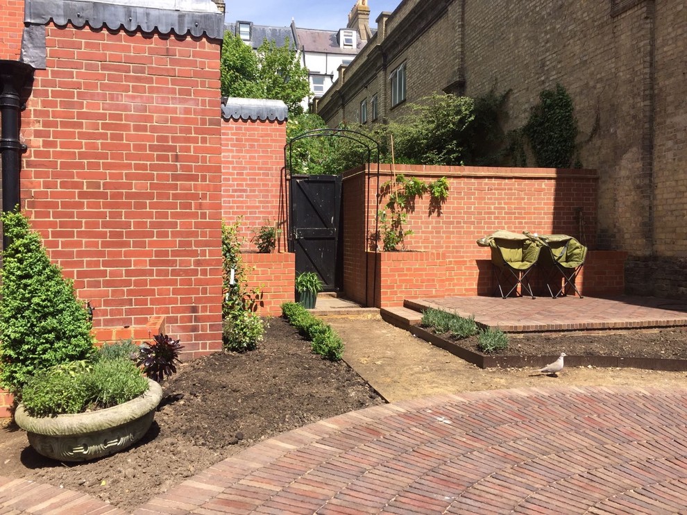Photo of a mid-sized traditional courtyard full sun formal garden for summer in Sussex with a vertical garden and brick pavers.