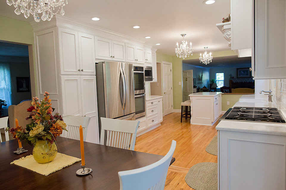 Photo of a large contemporary u-shaped eat-in kitchen in Boston with a farmhouse sink, louvered cabinets, white cabinets, white splashback, subway tile splashback, stainless steel appliances, medium hardwood floors and a peninsula.