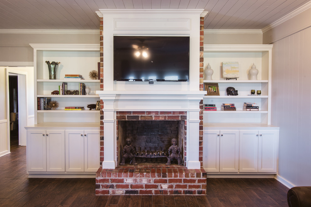 Mid-sized country formal open concept living room in New Orleans with beige walls, medium hardwood floors, a standard fireplace, a brick fireplace surround and a wall-mounted tv.