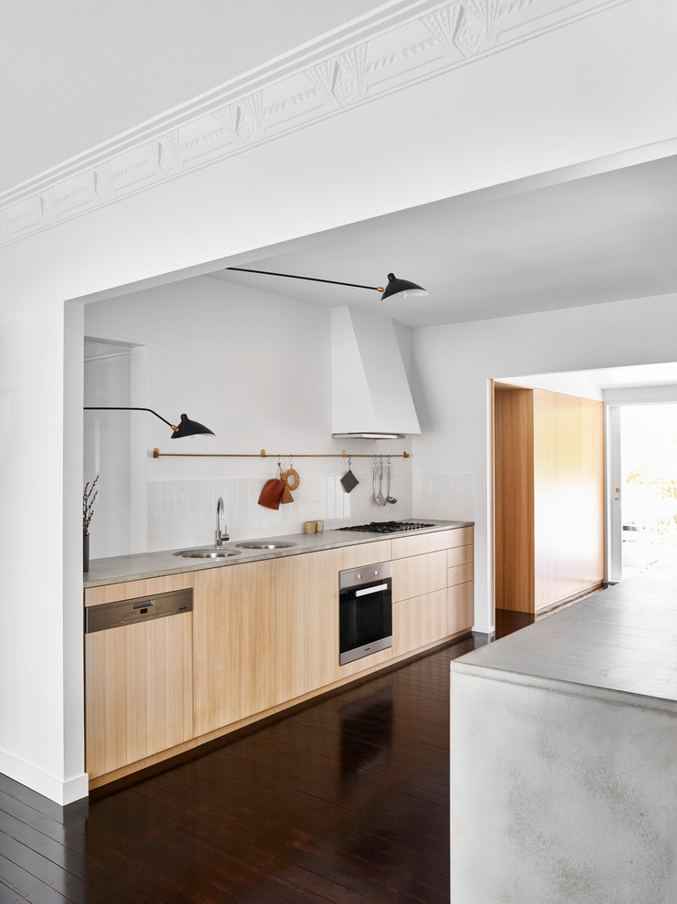 Photo of a small contemporary galley open plan kitchen with a double-bowl sink, light wood cabinets, concrete benchtops, white splashback, ceramic splashback, stainless steel appliances, dark hardwood floors, no island and black floor.