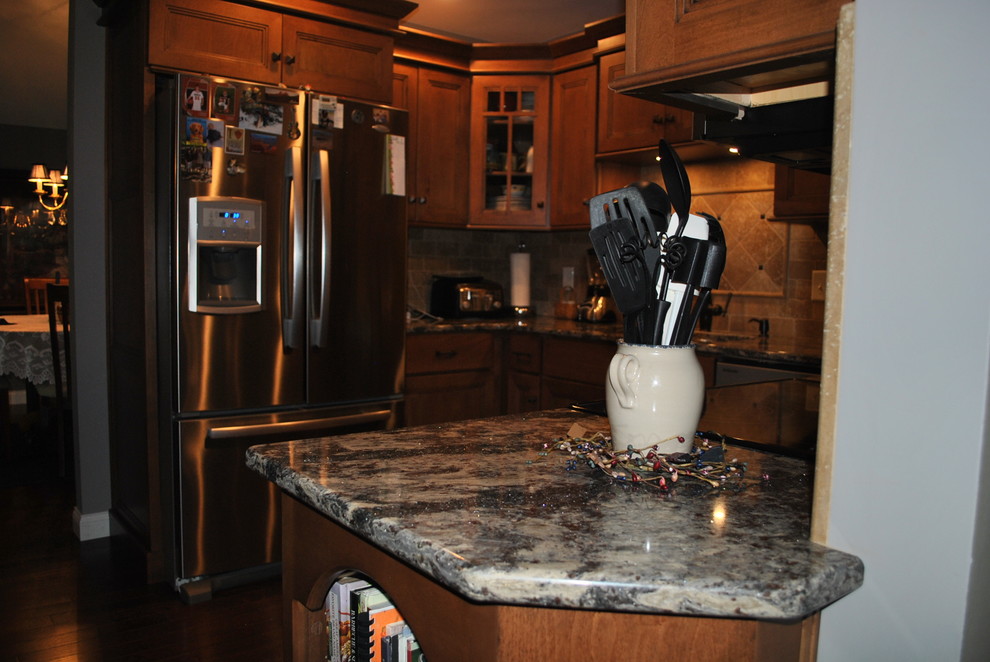Example of a brown floor kitchen design with brown cabinets, beige backsplash, stainless steel appliances, an island and gray countertops