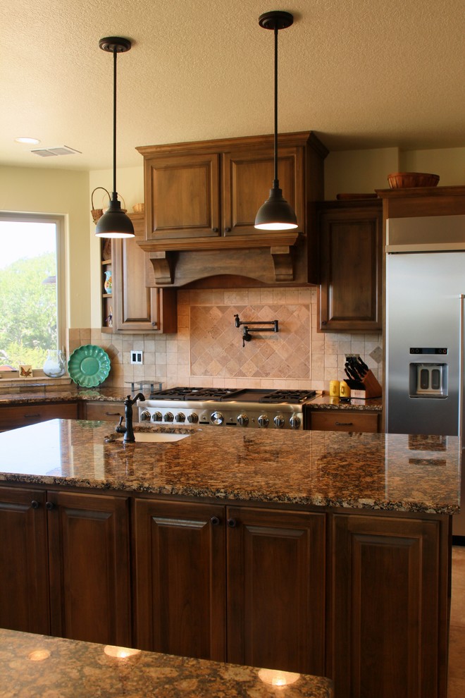 Eat-in kitchen - large southwestern u-shaped dark wood floor and brown floor eat-in kitchen idea in Austin with an undermount sink, raised-panel cabinets, dark wood cabinets, granite countertops, beige backsplash, travertine backsplash, stainless steel appliances, an island and multicolored countertops
