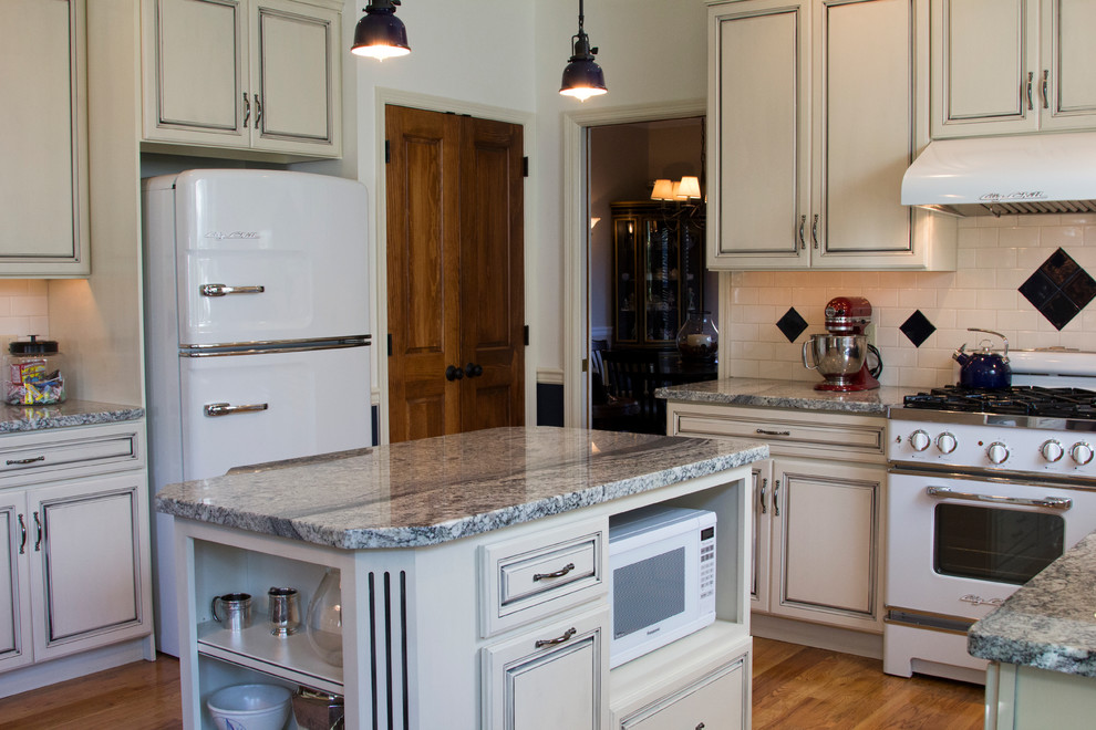 Inspiration for a mid-sized country u-shaped open plan kitchen in Philadelphia with a farmhouse sink, raised-panel cabinets, distressed cabinets, granite benchtops, beige splashback, subway tile splashback, white appliances, medium hardwood floors and with island.