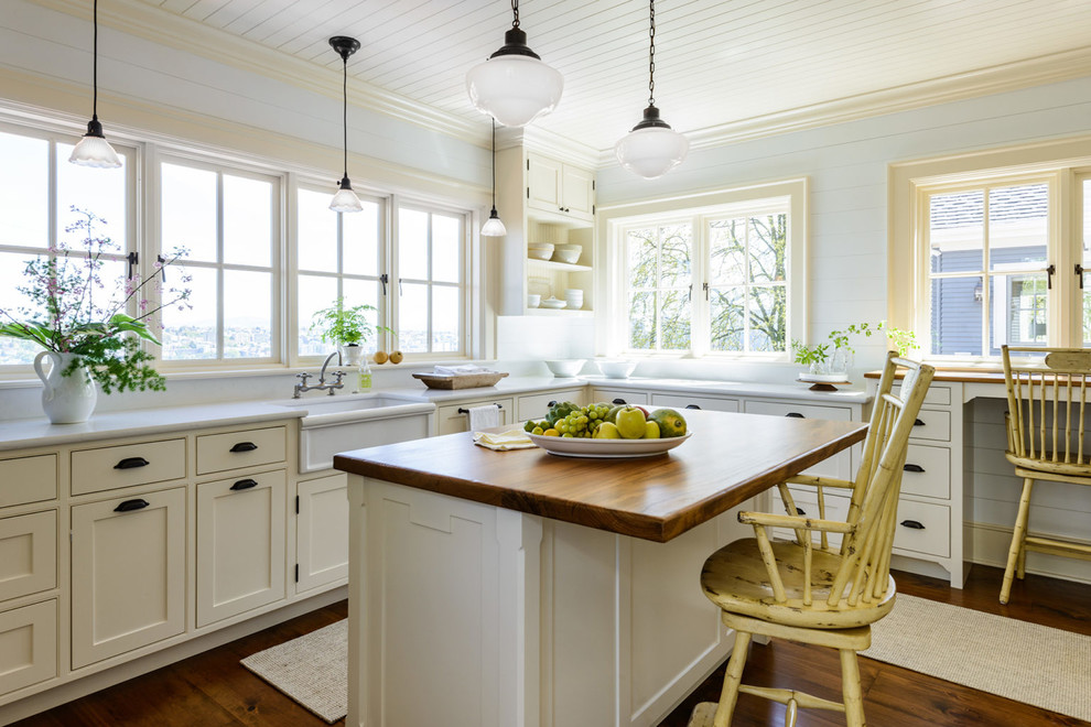 Design ideas for a traditional l-shaped kitchen in Seattle with a farmhouse sink, shaker cabinets, white cabinets, wood benchtops, white splashback, medium hardwood floors, with island, brown floor and brown benchtop.