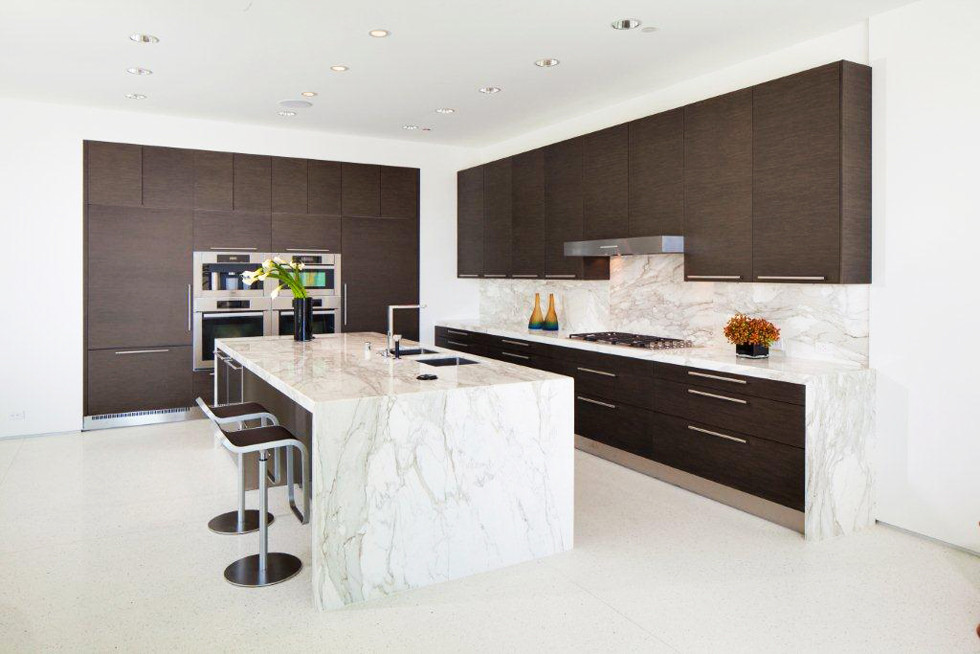 Design ideas for a mid-sized modern l-shaped open plan kitchen in Los Angeles with an undermount sink, flat-panel cabinets, dark wood cabinets, marble benchtops, white splashback, stone slab splashback, stainless steel appliances, concrete floors, with island, white floor and white benchtop.