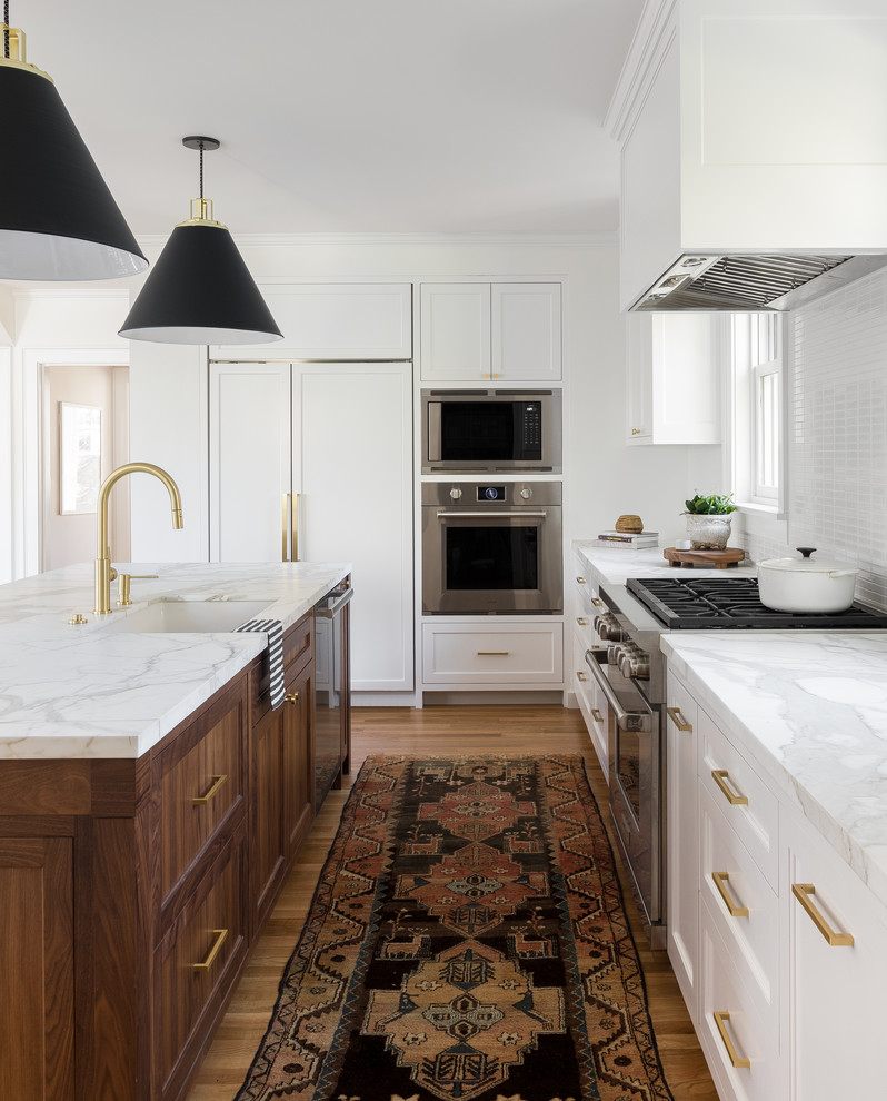 This is an example of a transitional l-shaped kitchen in Seattle with an undermount sink, shaker cabinets, white cabinets, white splashback, matchstick tile splashback, stainless steel appliances, light hardwood floors, with island and white benchtop.