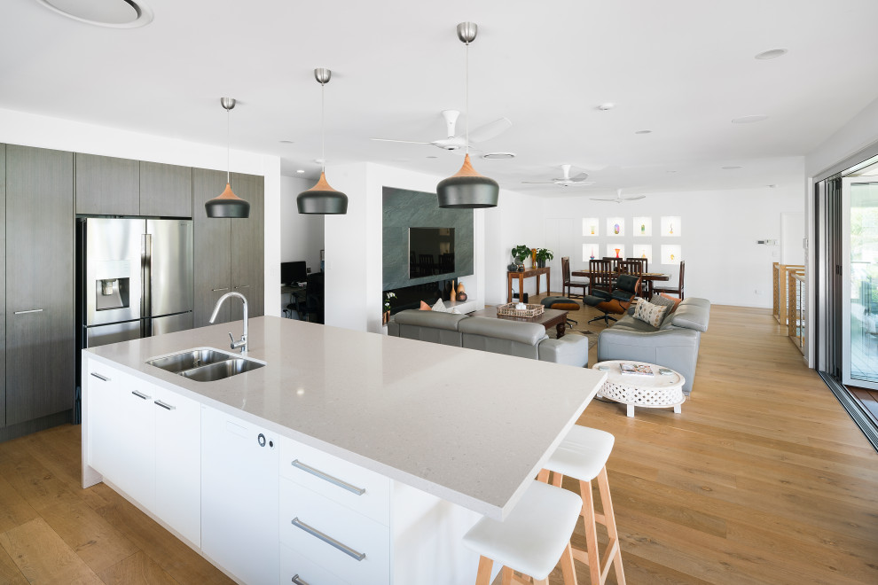 Design ideas for a mid-sized contemporary galley open plan kitchen in Brisbane with an undermount sink, flat-panel cabinets, white cabinets, quartz benchtops, white splashback, glass sheet splashback, stainless steel appliances, light hardwood floors, with island and white benchtop.