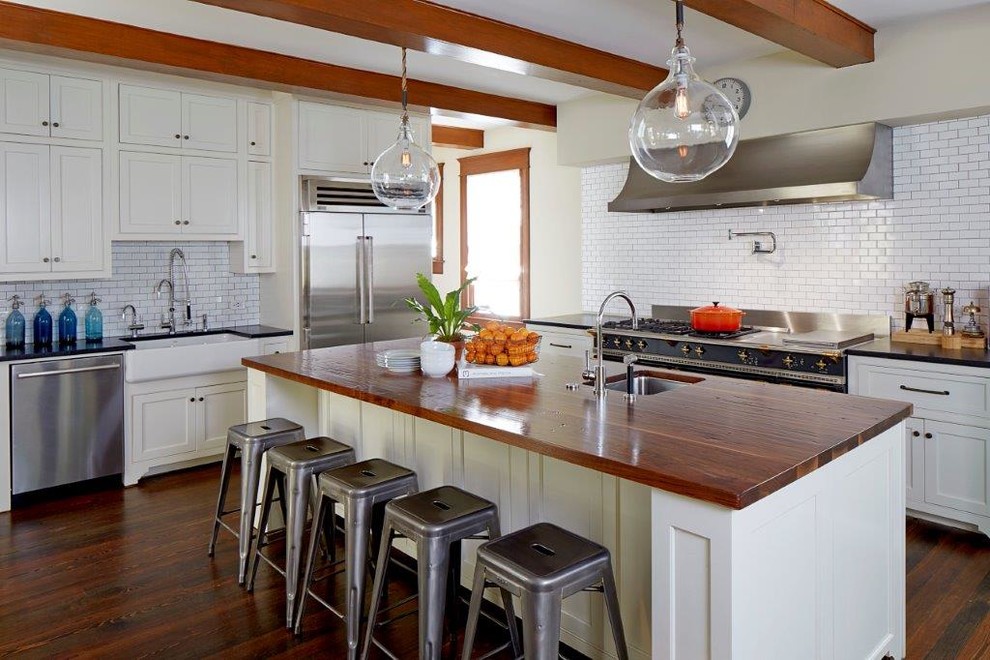 Photo of a mid-sized country l-shaped eat-in kitchen in Chicago with a farmhouse sink, shaker cabinets, white cabinets, soapstone benchtops, white splashback, subway tile splashback, stainless steel appliances, dark hardwood floors, with island and brown floor.