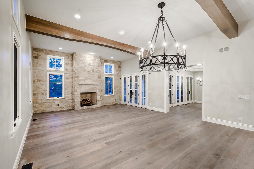 Photo of a large open concept living room in Denver with white walls, light hardwood floors, a standard fireplace, a stone fireplace surround, no tv and brown floor.