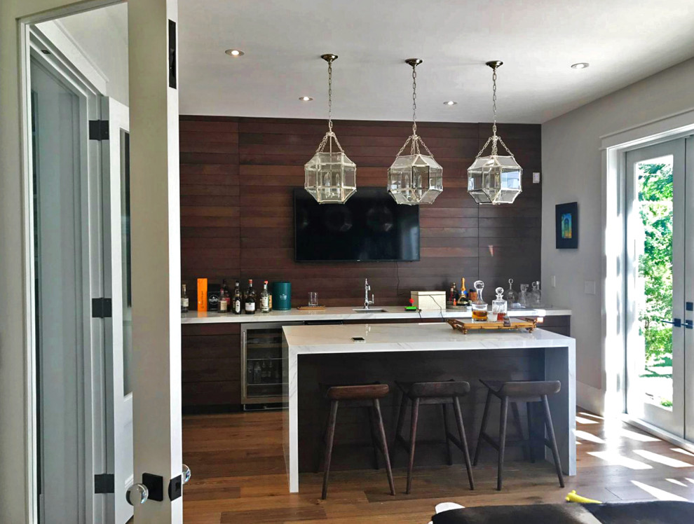 Photo of a large modern galley seated home bar in Miami with a drop-in sink, flat-panel cabinets, medium wood cabinets, quartz benchtops, brown splashback, shiplap splashback, medium hardwood floors, brown floor and white benchtop.