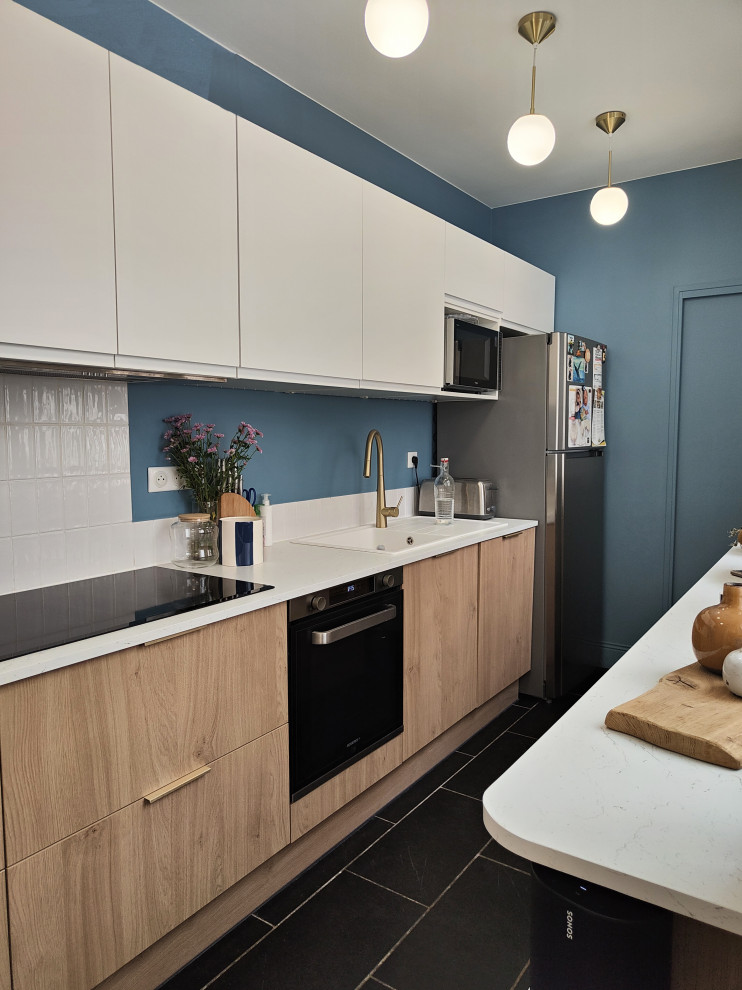 This is an example of a mid-sized transitional single-wall open plan kitchen in Lille with an undermount sink, flat-panel cabinets, light wood cabinets, laminate benchtops, white splashback, no island, black floor and white benchtop.