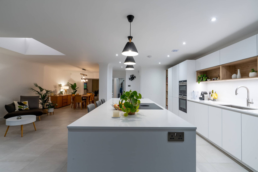 Photo of a large scandinavian galley open plan kitchen in Hertfordshire with flat-panel cabinets, white cabinets, quartzite benchtops, white splashback, black appliances, with island, white floor and white benchtop.