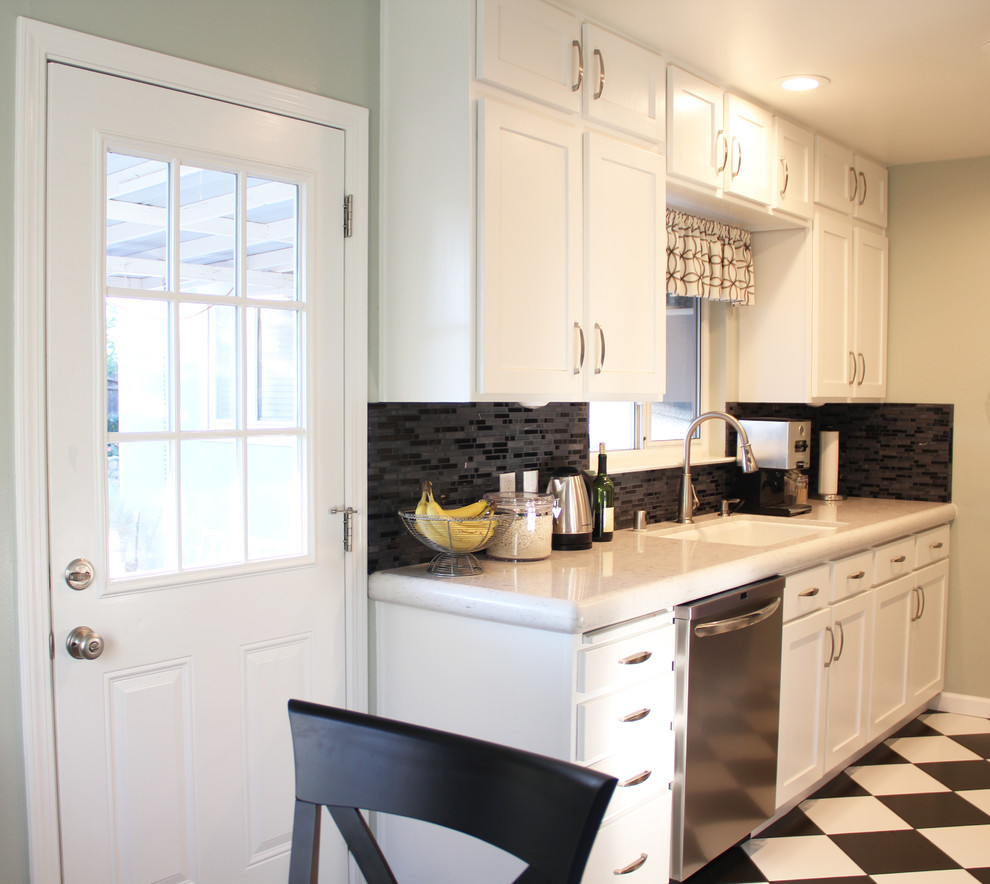 Small transitional galley eat-in kitchen in Sacramento with shaker cabinets, white cabinets, solid surface benchtops, black splashback, glass tile splashback, stainless steel appliances, no island, an undermount sink and vinyl floors.