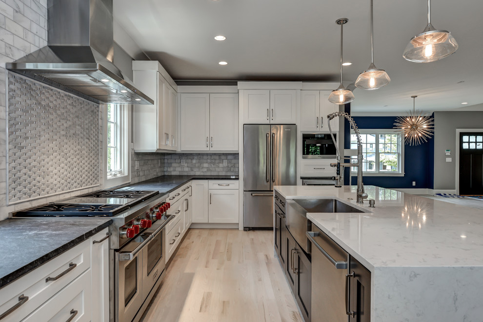 Inspiration for a large contemporary l-shaped kitchen in Atlanta with a farmhouse sink, shaker cabinets, white cabinets, soapstone benchtops, grey splashback, stone tile splashback, stainless steel appliances, light hardwood floors and with island.