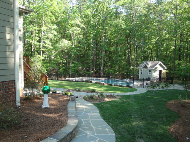 Photo of a large modern backyard kidney-shaped natural pool in Raleigh with a pool house and natural stone pavers.