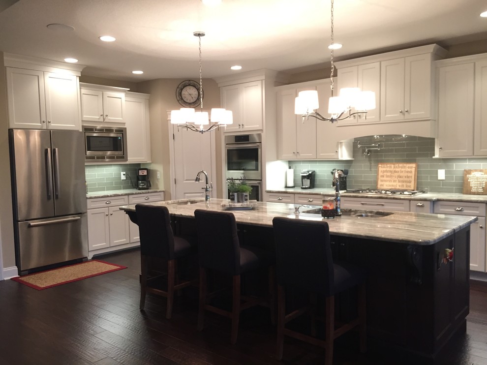 This is an example of a large transitional l-shaped kitchen in Nashville with an undermount sink, recessed-panel cabinets, white cabinets, granite benchtops, glass tile splashback, stainless steel appliances, dark hardwood floors, with island, grey splashback and brown floor.
