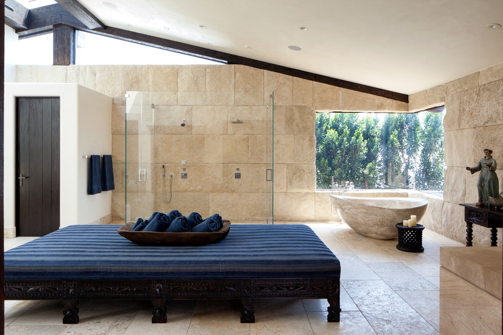 This is an example of a large mediterranean bathroom in Orange County with a freestanding tub, a curbless shower, beige tile, stone tile and beige walls.
