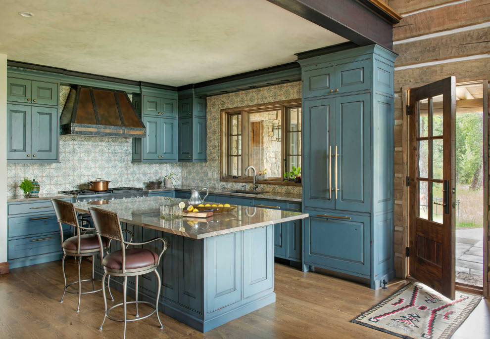 Country l-shaped kitchen in Other with an undermount sink, raised-panel cabinets, blue cabinets, multi-coloured splashback, panelled appliances, medium hardwood floors, with island, brown floor and grey benchtop.