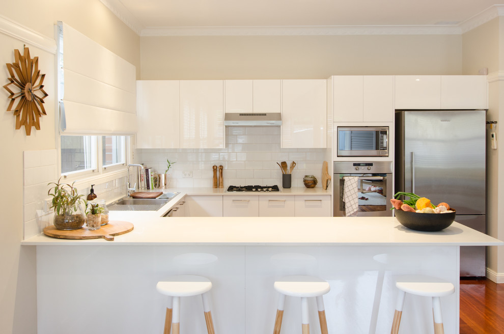 Photo of a mid-sized contemporary u-shaped kitchen in Sydney with a double-bowl sink, white cabinets, granite benchtops, white splashback, ceramic splashback, stainless steel appliances, dark hardwood floors and a peninsula.