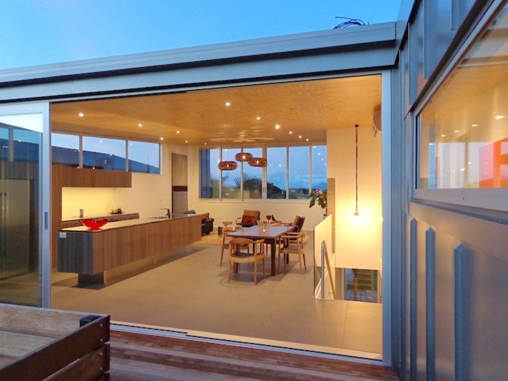 Inspiration for a mid-sized beach style galley eat-in kitchen in Auckland with an integrated sink, recessed-panel cabinets, medium wood cabinets, stainless steel benchtops, stainless steel appliances and with island.