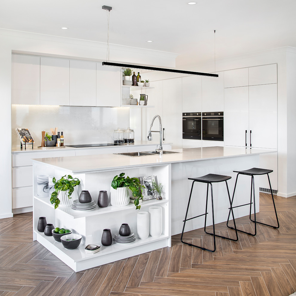 Photo of a contemporary l-shaped kitchen in Brisbane with a drop-in sink, flat-panel cabinets, with island, brown floor and white benchtop.