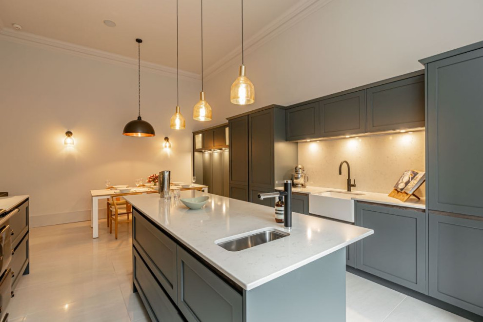 Large modern galley eat-in kitchen in Edinburgh with a farmhouse sink, recessed-panel cabinets, green cabinets, mirror splashback, black appliances, with island, white floor and white benchtop.