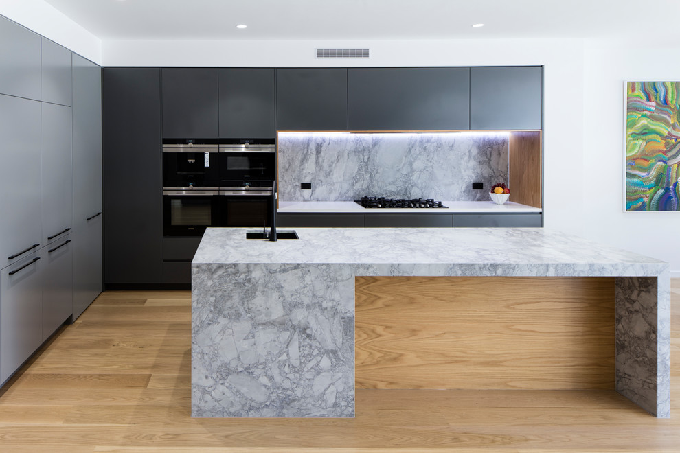 This is an example of a mid-sized contemporary galley open plan kitchen in Brisbane with a single-bowl sink, flat-panel cabinets, grey cabinets, granite benchtops, grey splashback, stone slab splashback, black appliances, laminate floors, with island and grey benchtop.