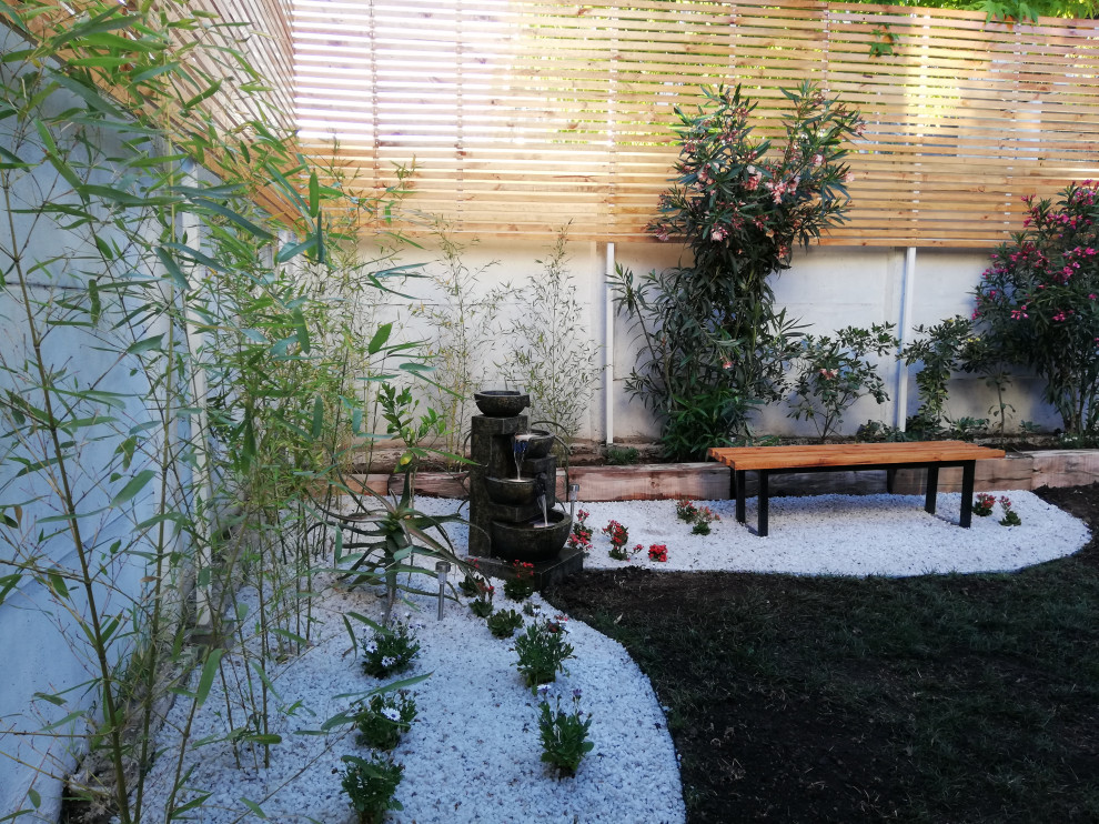 На фото: садовый фонтан среднего размера на заднем дворе в современном стиле с подъездной дорогой, полуденной тенью, покрытием из гальки и с деревянным забором