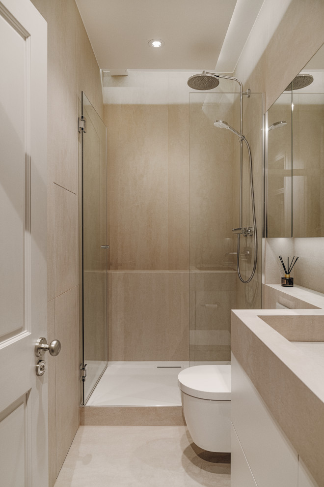 This is an example of a small eclectic shower room bathroom in London with glass-front cabinets, white cabinets, a walk-in shower, a wall mounted toilet, beige tiles, ceramic tiles, beige walls, ceramic flooring, a built-in sink, tiled worktops, beige floors, a hinged door, beige worktops, feature lighting, a single sink, a built in vanity unit and a drop ceiling.