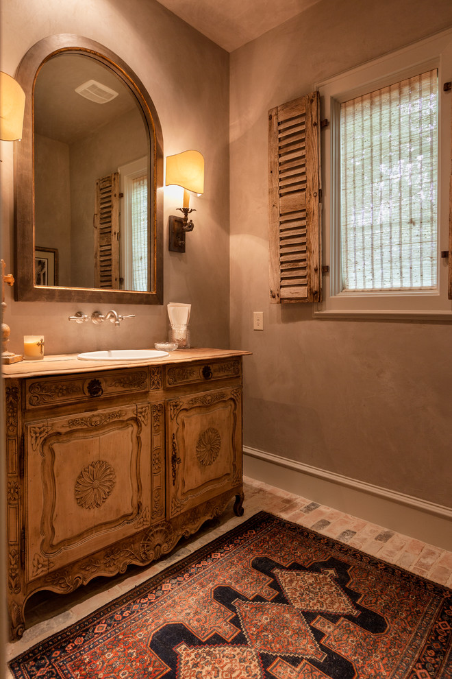 Inspiration for an expansive traditional powder room in Houston with raised-panel cabinets, medium wood cabinets, beige walls, brick floors and a console sink.