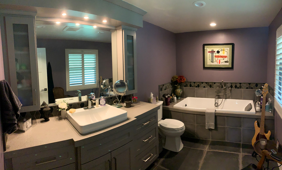This is an example of a mid-sized transitional master bathroom in Sacramento with shaker cabinets, grey cabinets, a drop-in tub, a two-piece toilet, gray tile, ceramic tile, purple walls, slate floors, a vessel sink, solid surface benchtops, grey floor and beige benchtops.