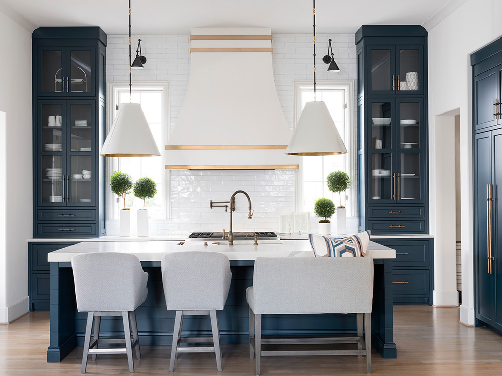 Inspiration for a transitional l-shaped kitchen in Atlanta with an undermount sink, shaker cabinets, blue cabinets, white splashback, subway tile splashback, stainless steel appliances, medium hardwood floors, with island, brown floor and white benchtop.