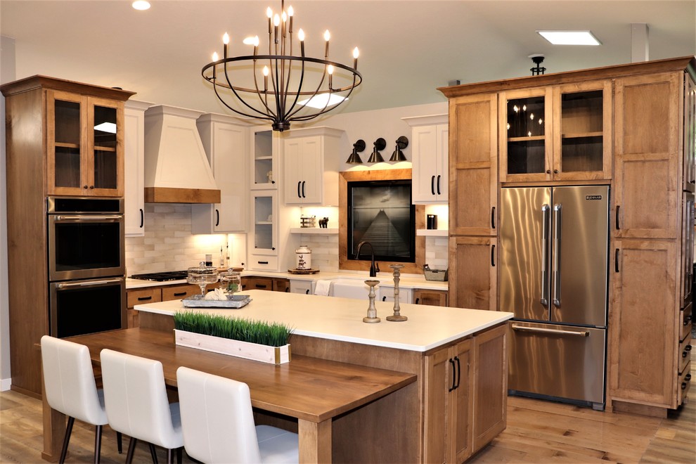 Photo of a mid-sized country l-shaped separate kitchen in Other with with island, a farmhouse sink, shaker cabinets, medium wood cabinets, quartz benchtops, beige splashback, subway tile splashback, stainless steel appliances, medium hardwood floors, brown floor and white benchtop.