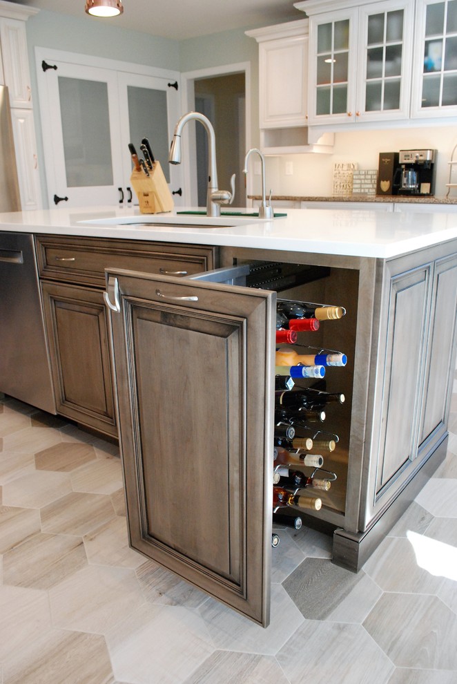 Mid-sized transitional l-shaped porcelain tile and beige floor enclosed kitchen photo in New York with an undermount sink, raised-panel cabinets, white cabinets, solid surface countertops, white backsplash, porcelain backsplash, stainless steel appliances and an island