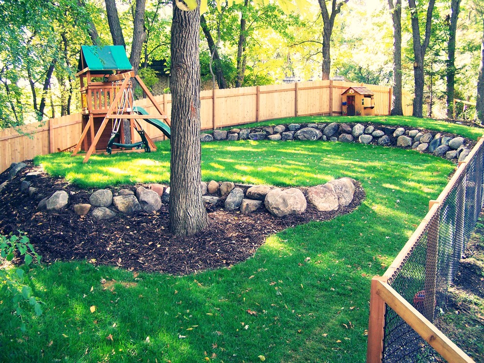 Large traditional backyard shaded garden in Minneapolis with with outdoor playset and mulch for summer.