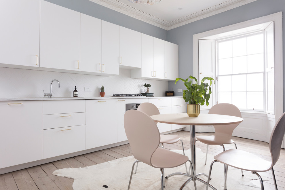 Photo of a mid-sized transitional single-wall eat-in kitchen in Edinburgh with a double-bowl sink, flat-panel cabinets, white cabinets, laminate benchtops, white splashback, ceramic splashback, panelled appliances, light hardwood floors, grey floor and white benchtop.