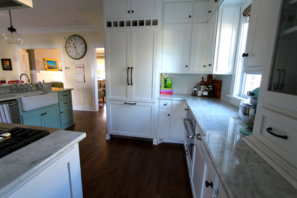 Inspiration for a transitional medium tone wood floor kitchen remodel in Omaha with a farmhouse sink, shaker cabinets, white cabinets, quartzite countertops, white backsplash, ceramic backsplash, stainless steel appliances and a peninsula
