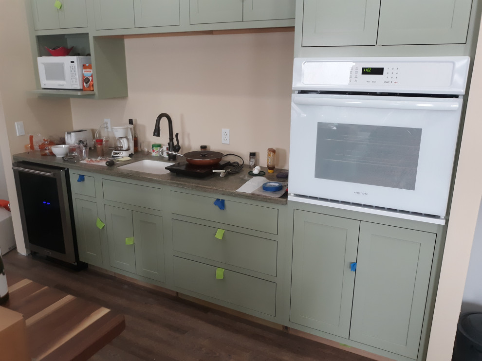 Large traditional l-shaped open plan kitchen in Other with an integrated sink, shaker cabinets, medium wood cabinets, solid surface benchtops, white appliances, vinyl floors, with island, brown floor and green benchtop.