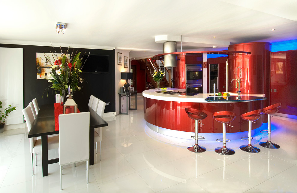 Design ideas for an expansive modern kitchen/diner in London with an integrated sink, flat-panel cabinets, red cabinets, composite countertops, blue splashback, glass sheet splashback, stainless steel appliances, porcelain flooring and an island.