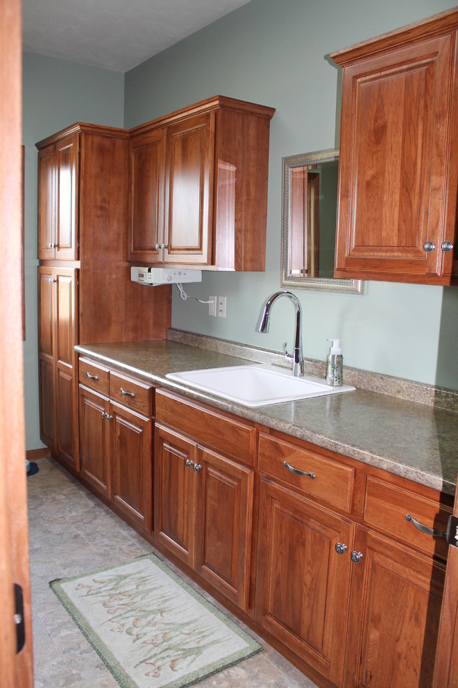 Photo of a mid-sized traditional single-wall utility room in Other with a single-bowl sink, raised-panel cabinets, medium wood cabinets, laminate benchtops, blue walls and a side-by-side washer and dryer.